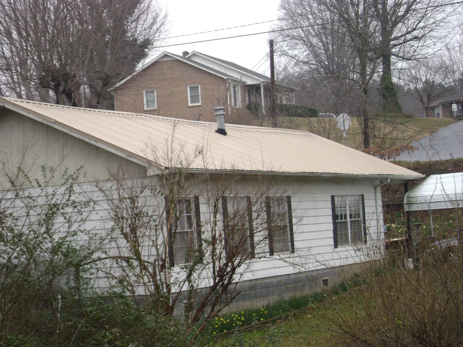 Tan metal roof on a white sided house set into a hillside — Commercial Roofing by Roofing Brothers in Covington